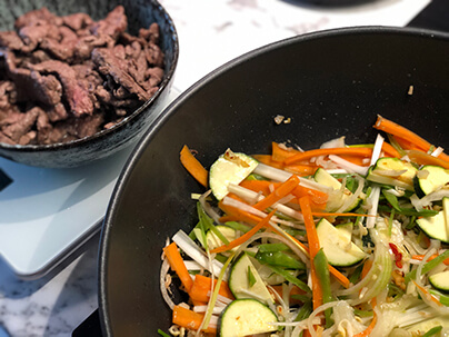 grönsaker wokas i en wokpanna och älgwok ligger i en liten skål på sidan